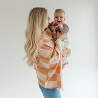 Woman holding a baby wrapped in a checkered blanket against a plain background