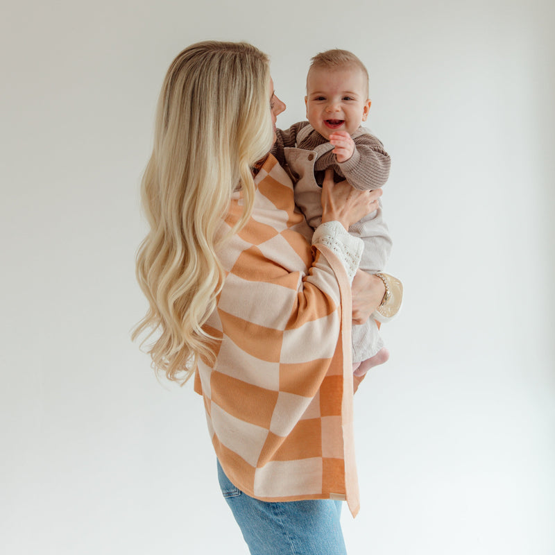 Woman holding a baby wrapped in a checkered blanket against a plain background