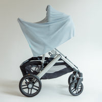 A light blue baby stroller canopy cover draped over a silver and black stroller frame, set against a plain light gray studio background.